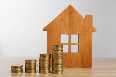 Photo of Mortgage concept. Model house and stacks of coins on wooden table against light grey background