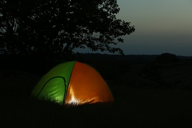Photo of Modern tent lit from inside in wilderness at night, space for text. Overnight camping