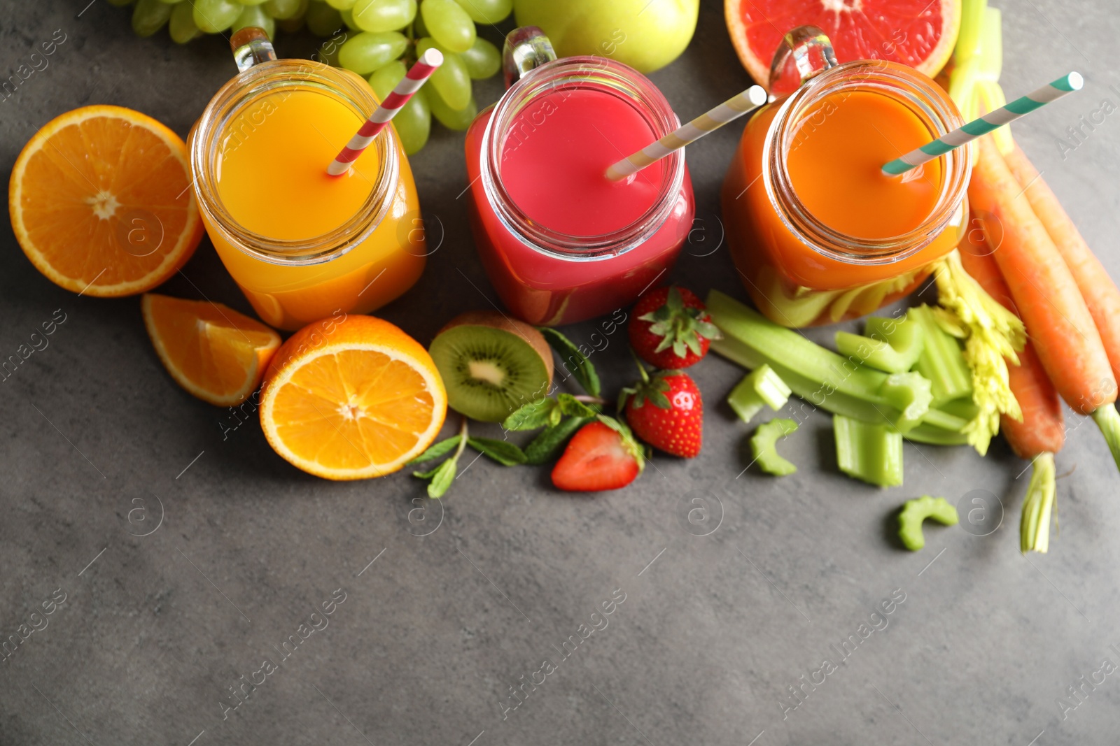 Photo of Different juices in mason jars and fresh ingredients on grey background, top view. Space for text