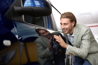 Photo of Young man near new car in modern auto dealership