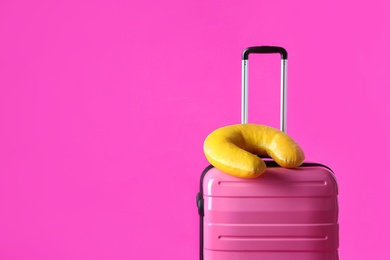 Photo of Suitcase and yellow travel pillow on pink background, space for text