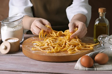 Photo of Woman making homemade pasta at wooden table, closeup