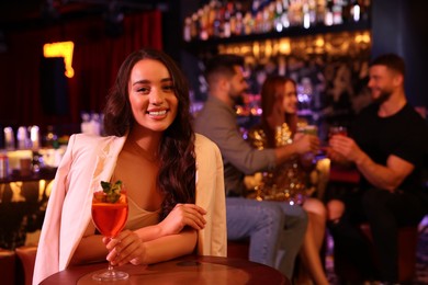 Photo of Friends spending time together in bar. Beautiful woman with fresh alcoholic cocktail at table, space for text