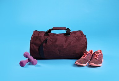 Photo of Red sports bag, sneakers and dumbbells on light blue background