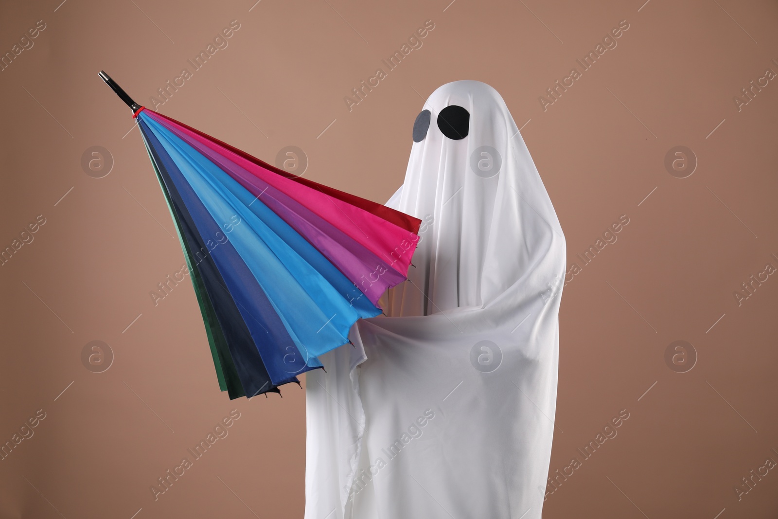 Photo of Person in ghost costume with color umbrella on dark beige background
