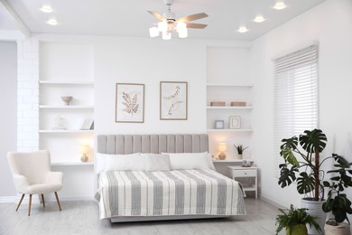 Photo of Comfortable furniture, ceiling fan, houseplants and accessories in stylish bedroom