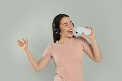 Photo of Happy woman in headphones enjoying music and singing into smartphone on grey background