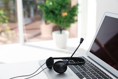 Photo of Modern laptop and headset on table indoors. Technical support concept