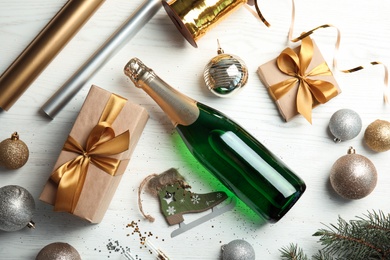 Photo of Christmas composition with bottle of champagne and gifts on wooden background, top view