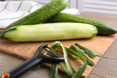Photo of Fresh cucumbers, peels and peeler on wooden table, closeup