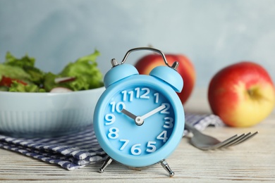 Photo of Alarm clock and healthy food on white wooden table. Meal timing concept
