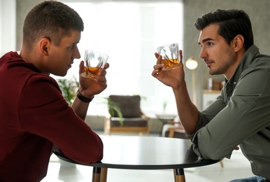 Photo of Young men drinking whiskey together at home