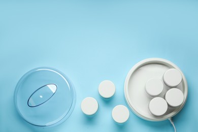 Photo of Modern yogurt maker with jars on light blue background, flat lay. Space for text
