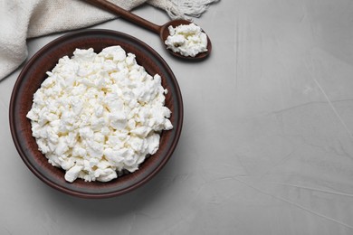 Photo of Clay bowl and spoon with cottage cheese on grey table, flat lay. Space for text