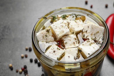 Jar with feta cheese marinated in oil on grey table, closeup. Pickled food