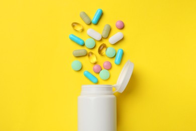 Photo of Different vitamin pills and bottle on yellow background, top view.