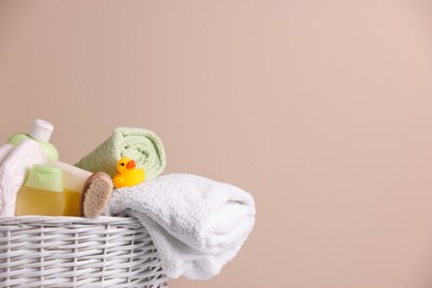 Photo of Wicker basket with baby cosmetic products, bath accessories and rubber duck on beige background. Space for text