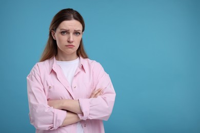 Photo of Portrait of sad woman with crossed arms on light blue background, space for text