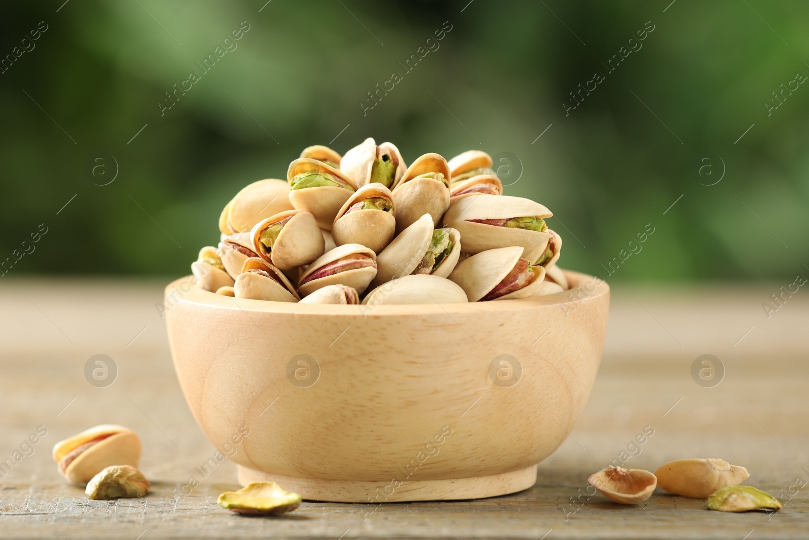 Photo of Tasty pistachios in bowl on wooden table against blurred background, closeup