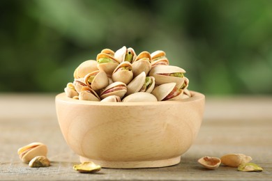 Photo of Tasty pistachios in bowl on wooden table against blurred background, closeup