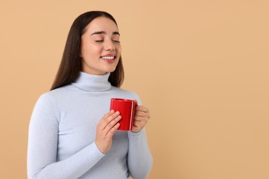 Happy young woman holding red ceramic mug on beige background, space for text