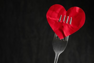Photo of Broken heart. Red paper heart pierced with fork against black background, closeup. Space for text