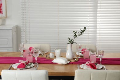 Photo of Color accent table setting. Glasses, plates, pink napkins and vase with green branch in dining room