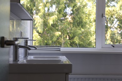 Photo of White clean sinks with water taps near window in bathroom