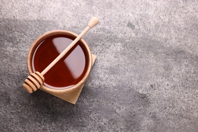 Photo of Delicious honey in bowl and dipper on grey textured table, top view. Space for text