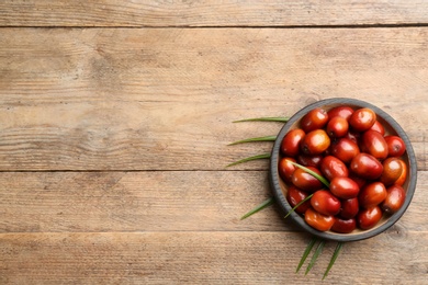 Palm oil fruits in bowl on wooden table, flat lay. Space for text