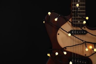 Photo of Guitar with golden lights on black background, space for text. Christmas music