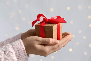 Photo of Woman holding gift box with red bow against blurred festive lights, closeup. Bokeh effect