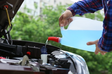Photo of Man pouring liquid from plastic canister into car washer fluid reservoir, closeup