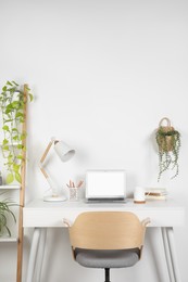 Photo of Cozy workspace with laptop, lamp and stationery on wooden desk at home