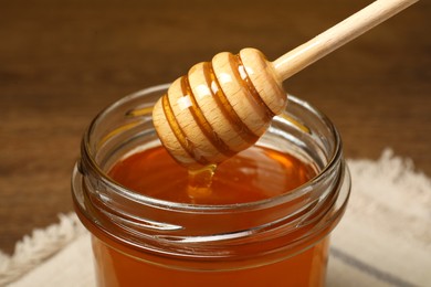 Photo of Pouring honey from dipper into jar at table, closeup
