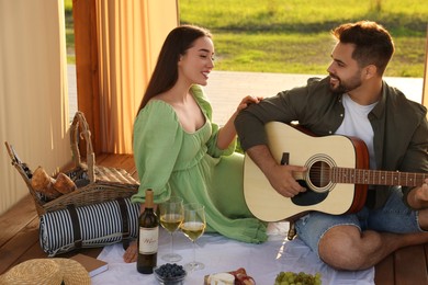 Photo of Romantic date. Beautiful woman listening to her boyfriend playing guitar during picnic outdoors