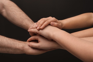 Photo of Young people putting their hands together on dark background, closeup