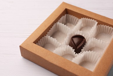 Photo of Partially empty box of chocolate candies on white wooden table, closeup