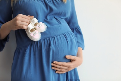 Photo of Pregnant woman holding baby booties near tummy on light background, closeup. Space for text