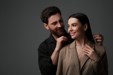 Photo of Man putting elegant necklace on beautiful woman against dark grey background