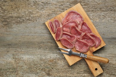 Photo of Board with slices of raw beef tongue carving fork on wooden table, top view. Space for text