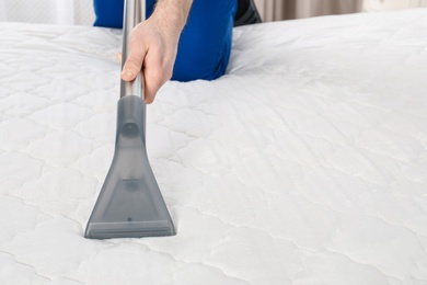 Photo of Man disinfecting mattress with vacuum cleaner, closeup. Space for text