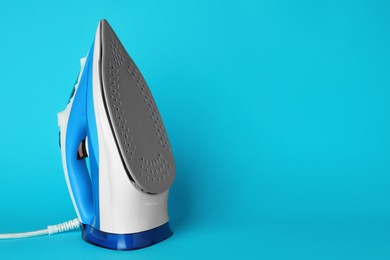 Photo of One modern iron on light blue background, space for text. Home appliance