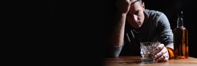 Image of Suffering from hangover. Man with alcoholic drink at table against black background, selective focus. Banner design with space for text