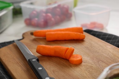 Photo of Wooden board with carrots, knife and containers on table, closeup. Food storage