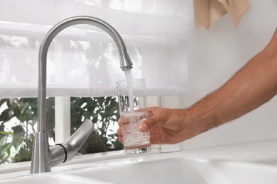 Photo of Man filling glass with water from tap at home, closeup