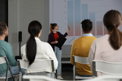 Photo of Female business trainer giving lecture in conference room with projection screen