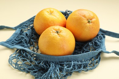 Photo of String bag with oranges on beige background, closeup