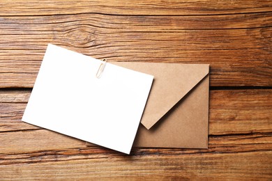 Photo of Blank sheet of paper, paperclip and letter envelope on wooden table, top view. Space for text