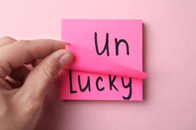 Photo of Woman holding notes with word UNLUCKY on pink background, top view